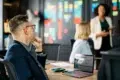 Business professionals in a meeting with a presentation on a laptop and colorful sticky notes on a wall.