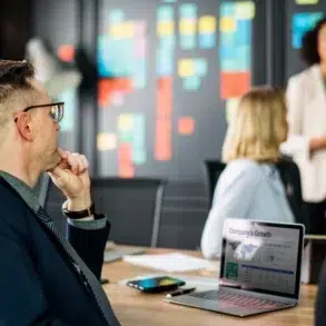 Business professionals in a meeting with a presentation on a laptop and colorful sticky notes on a wall.