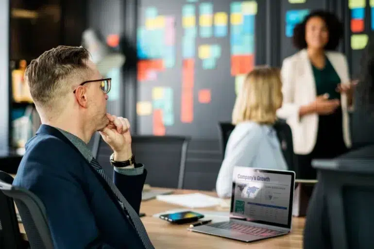 Business professionals in a meeting with a presentation on a laptop and colorful sticky notes on a wall.