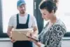 A delivery person holds a box while a woman signs a document on a clipboard.