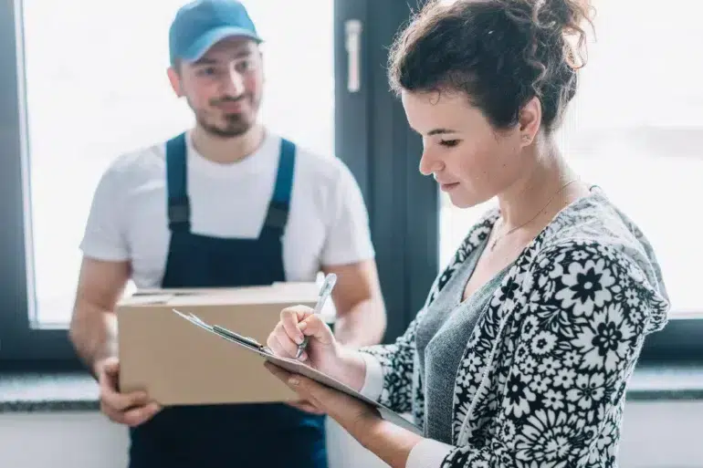 A delivery person holds a box while a woman signs a document on a clipboard.