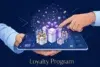 A finger points to a large gift box on a smartphone screen displaying a loyalty program with surrounding smaller gift boxes and sparkling confetti.