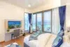 Modern hotel room with a bed, desk, TV, and a large window overlooking a turquoise ocean with balconies.