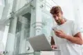 Man using smartphone and laptop with a WiFi icon overlayed.