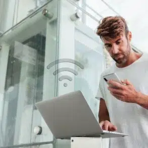 Man using smartphone and laptop with a WiFi icon overlayed.