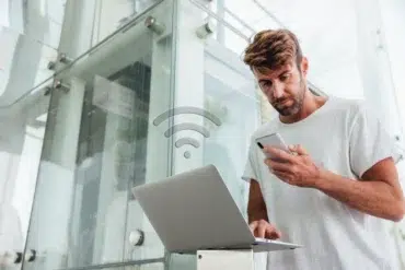Man using smartphone and laptop with a WiFi icon overlayed.