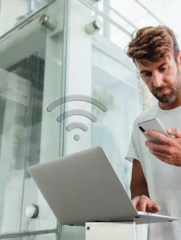 Man using smartphone and laptop with a WiFi icon overlayed.
