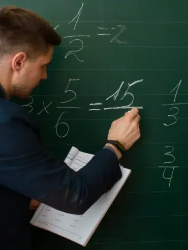 Teacher explains fractions on a chalkboard to a young student.