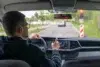 Man driving a car on a rainy day, pointing at the dashboard.