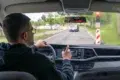 Man driving a car on a rainy day, pointing at the dashboard.