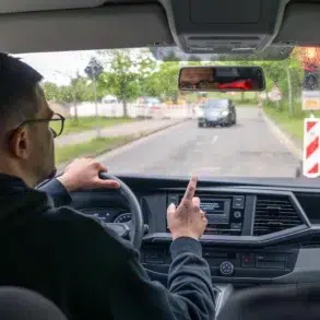Man driving a car on a rainy day, pointing at the dashboard.
