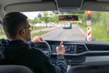 Man driving a car on a rainy day, pointing at the dashboard.