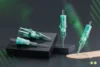 Three green and clear tattoo needle cartridges are displayed on black pedestals against a dark background.