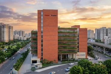 Modern brick hospital building with green vertical gardens at sunset in a cityscape.
