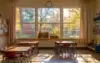 Classroom with desks and chairs facing a large window showing colorful autumn foliage.