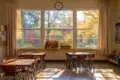 Classroom with desks and chairs facing a large window showing colorful autumn foliage.
