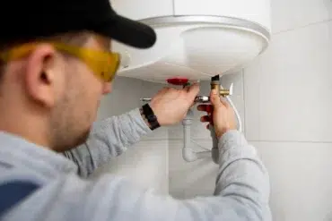Plumber in safety glasses working on a water heater connection.