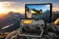 Rugged tablet on a rocky mountain top at sunset, displaying an image of a skydiver. Orange tent and distant peaks enhance the adventurous mood.