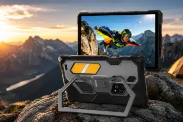Rugged tablet on a rocky mountain top at sunset, displaying an image of a skydiver. Orange tent and distant peaks enhance the adventurous mood.