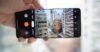 A hand holds a smartphone horizontally, displaying the camera app interface capturing an ultra-wide view of a dense urban street scene with tall buildings.