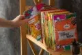 Hand selects a colorful comic book from a shelf filled with many comic books.