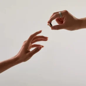Two hands reach out, one offering a small ring while the other receives it.