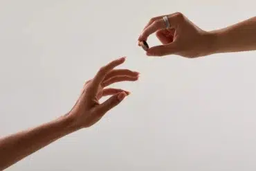 Two hands reach out, one offering a small ring while the other receives it.