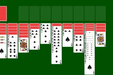A game of Solitaire is set up with seven columns of face-down and face-up playing cards on a green background.