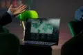 A person gestures while looking at a laptop screen displaying a world map with data visualizations.