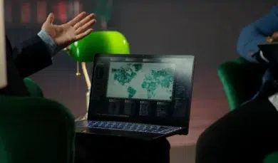 A person gestures while looking at a laptop screen displaying a world map with data visualizations.