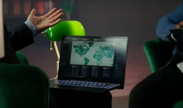 A person gestures while looking at a laptop screen displaying a world map with data visualizations.