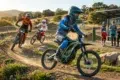 Electric dirt bikers race on a dirt track with a solar-powered charging station in the background.