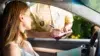 A woman in a car receiving a traffic ticket from a police officer writing on a clipboard outside the driver's window.