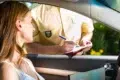 A woman in a car receiving a traffic ticket from a police officer writing on a clipboard outside the driver's window.