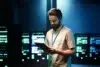 Man with beard in tan shirt holding tablet in front of glowing server racks.