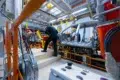 Workers operate on the aluminum car body chassis on an automotive assembly line.
