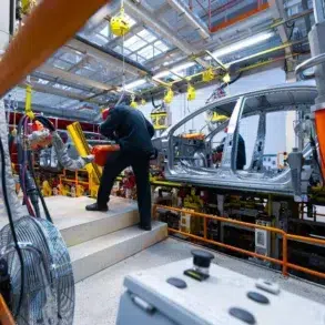 Workers operate on the aluminum car body chassis on an automotive assembly line.