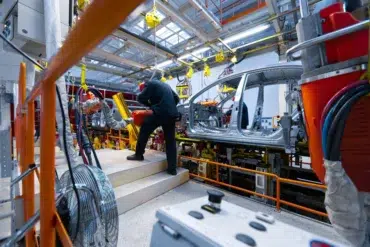 Workers operate on the aluminum car body chassis on an automotive assembly line.