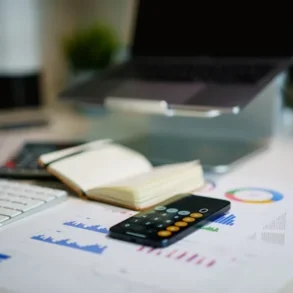 Desk with laptop, keyboard, open notebook, calculator, and financial charts.