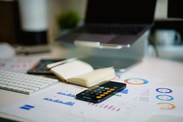 Desk with laptop, keyboard, open notebook, calculator, and financial charts.