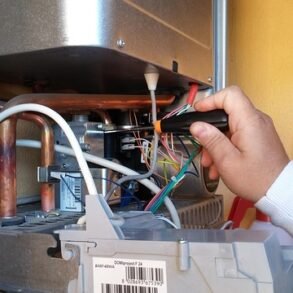 Technician's hand connecting wires inside a boiler.