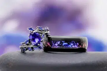 A purple gemstone engagement ring sits next to a black ring with a galaxy inlay.
