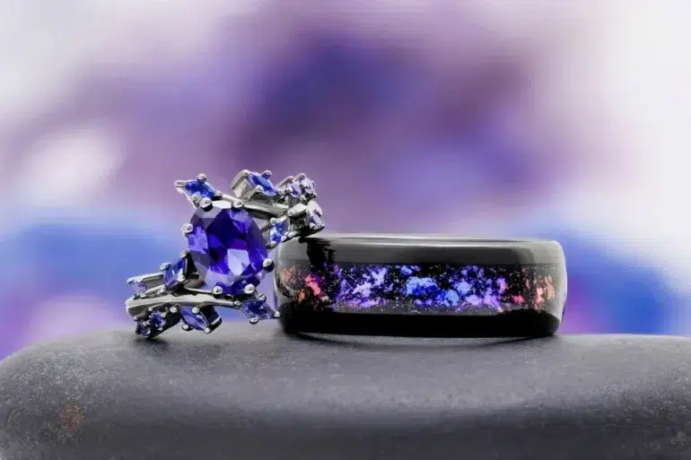 A purple gemstone engagement ring sits next to a black ring with a galaxy inlay.
