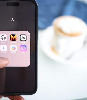 A person holds a smartphone displaying an "AI" folder with various app icons. In the blurred background, a cup of coffee sits on a table, creating a casual tone.