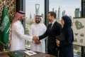Four businesspeople, including two men in Saudi attire, shake hands beside a Saudi flag, with Riyadh’s skyline visible through the windows.