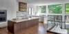 Modern open-plan kitchen with a marble island, wood cabinetry, stainless-steel appliances, and large windows overlooking lush greenery.