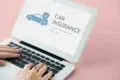 Hands typing on a laptop displaying a blue car with a shield and the words “CAR INSURANCE” on a pink background.