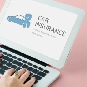 Hands typing on a laptop displaying a blue car with a shield and the words “CAR INSURANCE” on a pink background.