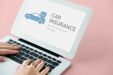 Hands typing on a laptop displaying a blue car with a shield and the words “CAR INSURANCE” on a pink background.