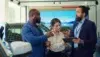 Three adults discuss a car in a showroom, with one man holding a tablet and the woman holding a takeaway cup.